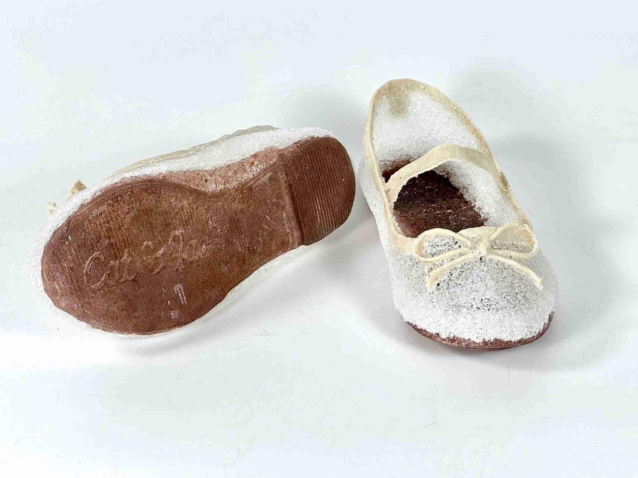 Delicate glass shoes - tiny off white bow and strap across a sparkly white surface, with brown soles.