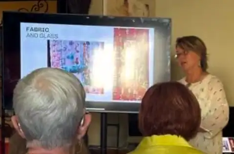 Woman with a large screen TV presentation, can see back of heads of audience members