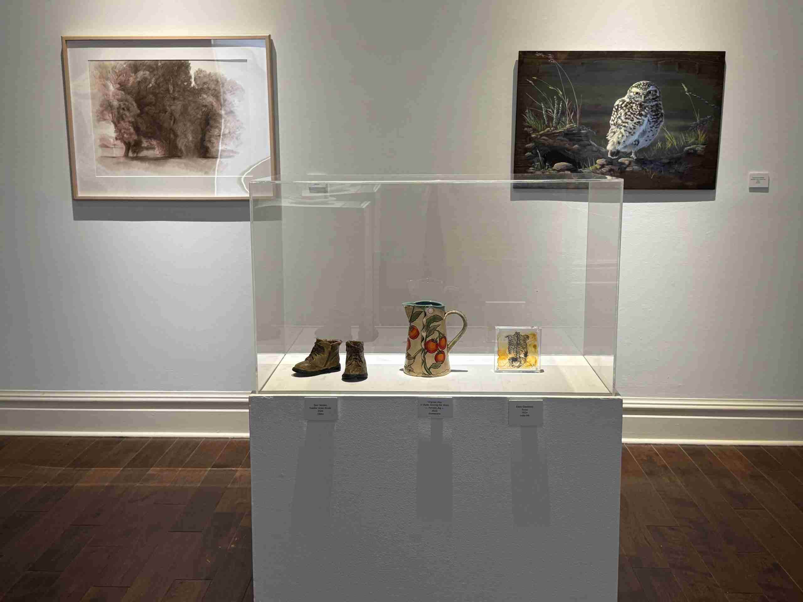 Pair of glass toddler boots next to a ceramic pitcher and a piece of art